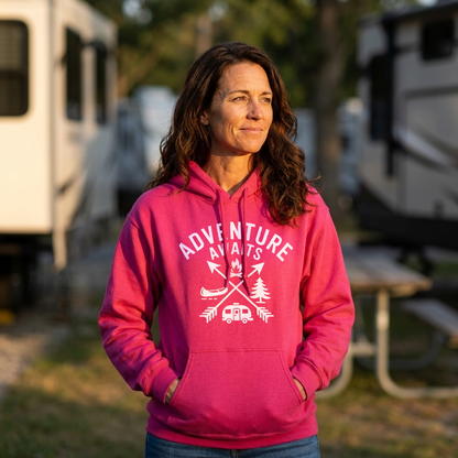 Woman in a bright pink Adventure Awaits camping hoodie standing in an RV campground with her hands in the pocket