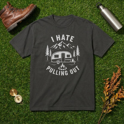 Dark charcoal gray I Hate Pulling Out t-shirt with a camper, mountains, and trees graphic laid flat on green grass with a leather boot, water bottle, compass, and dried leaves.