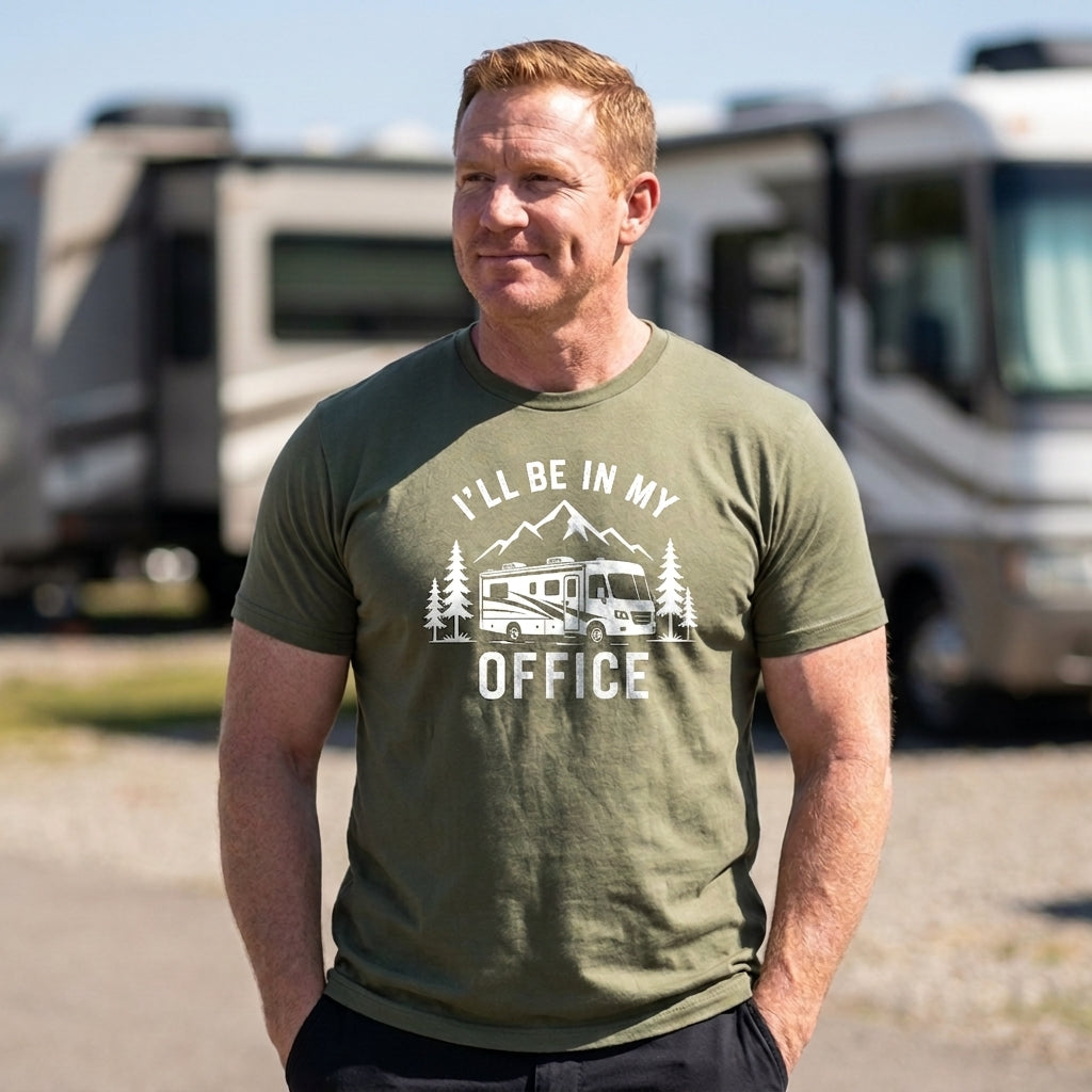 A man wearing an olive green graphic t-shirt that reads 'I'M SEXY AND I TOW IT' with a small truck and RV illustration, standing outdoors with RVs blurred in the background.