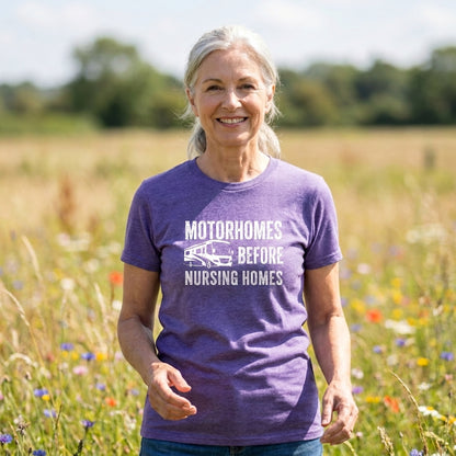 Smiling woman with gray hair in a heather purple Motorhomes Before Nursing Homes t-shirt in a wildflower field.