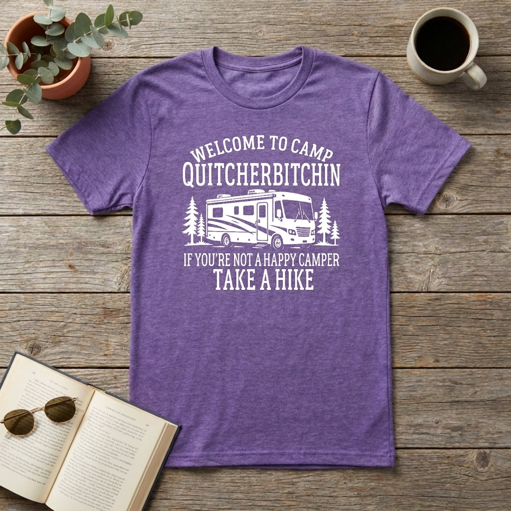 Heather purple Welcome to Camp Quitcherbitchin t-shirt with an RV and trees laid flat on a wooden surface with a plant, coffee mug, and open book.