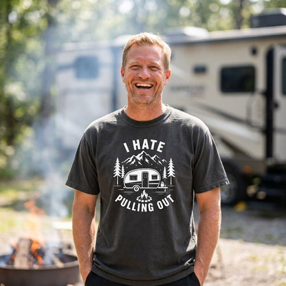 A man smiling outdoors in front of an RV, wearing a dark charcoal gray t-shirt with a white graphic that reads 'I HATE PULLING OUT' with mountains, trees, and a camper illustration.