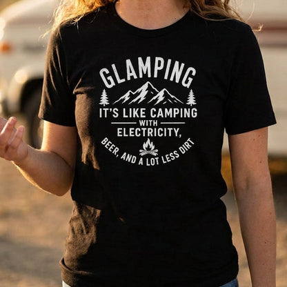A woman wearing a black short-sleeve graphic t-shirt with a white printed design that reads 'GLAMPING IT'S LIKE CAMPING WITH ELECTRICITY, BEER, AND A LOT LESS DIRT' with mountain and campfire illustrations.