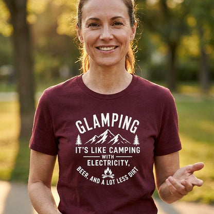 A woman smiling outdoors wearing a maroon short-sleeve t-shirt with a white graphic print that reads 'GLAMPING IT'S LIKE CAMPING WITH ELECTRICITY' and 'BEER AND A LOT LESS DRINK'.