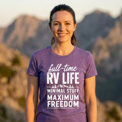 Smiling woman in a purple full-time RV life t-shirt reading minimal stuff, maximum freedom, with a mountain landscape behind her at sunset.