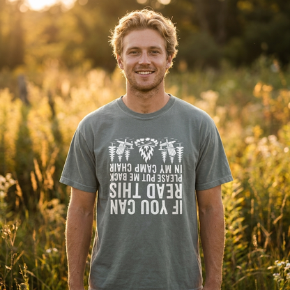 Smiling man in a heather gray If You Can Read This camp chair t-shirt with white text and bee illustrations, standing in a sunlit grassy field.