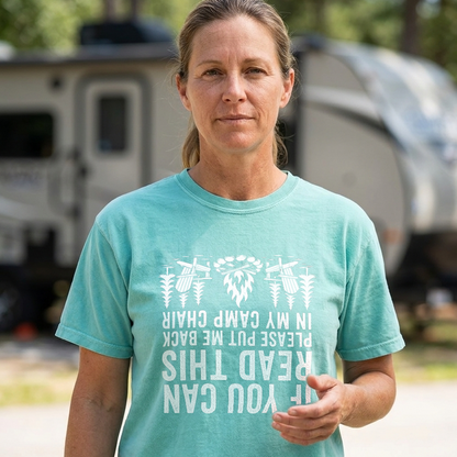 Woman in a teal If You Can Read This camp chair t-shirt with white text, standing outdoors in front of a blurred RV and trees.