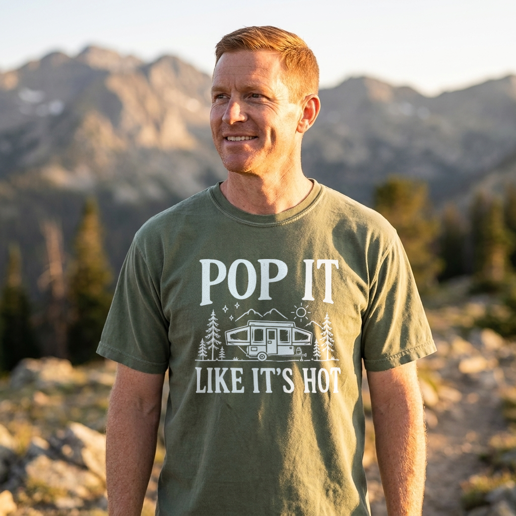 A man wearing an olive green t-shirt with a white graphic that reads 'POP IT LIKE IT'S HOT' and shows a mountain landscape in the background.