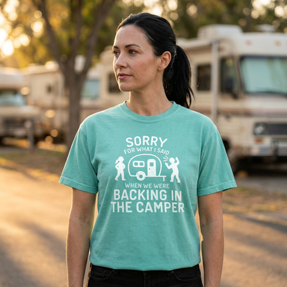 A woman wearing a mint green graphic t-shirt with a white print that reads 'POP IT LIKE IT'S HOT' and features a camper trailer design, standing outdoors in front of a blurred background of RVs and trees.