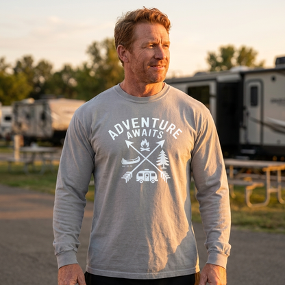Man in a light gray Adventure Awaits long sleeve camping shirt standing in an RV campground at sunset