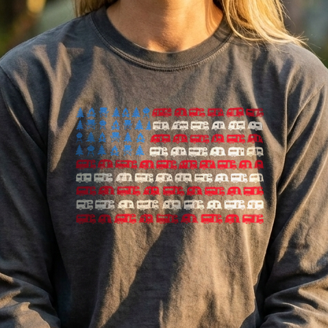 Smiling woman at a campsite picnic table in a charcoal gray long sleeve shirt with an RV American flag design