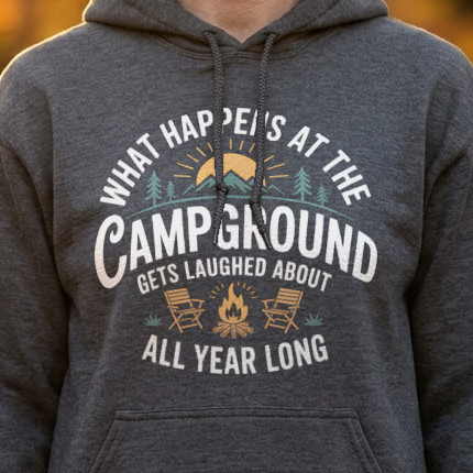 Close-up of a dark gray hoodie with a white What Happens at the Campground Gets Laughed About All Year Long design against golden autumn leaves