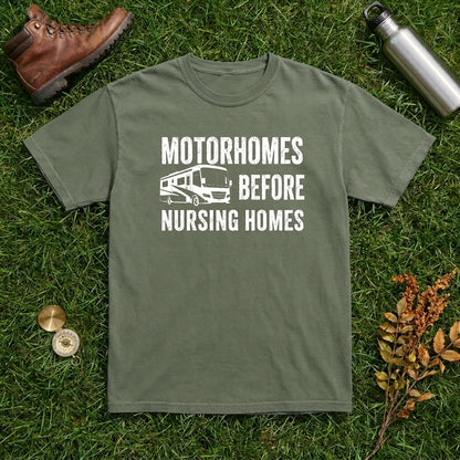 Olive green Motorhomes Before Nursing Homes t-shirt laid flat on grass with a boot, water bottle, and dried leaves.